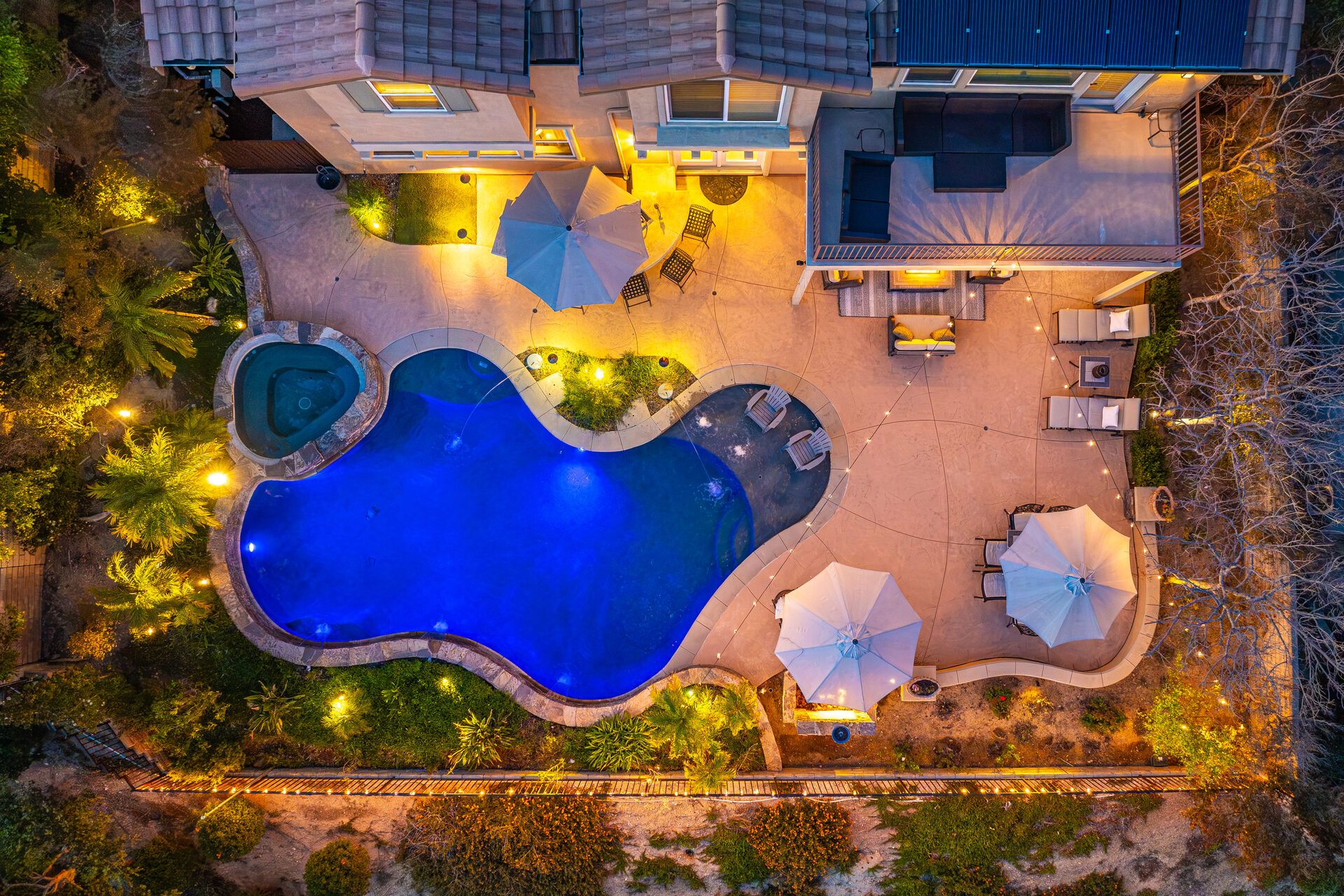 Top-down twilight aerial view of the illuminated pool and outdoor entertaining